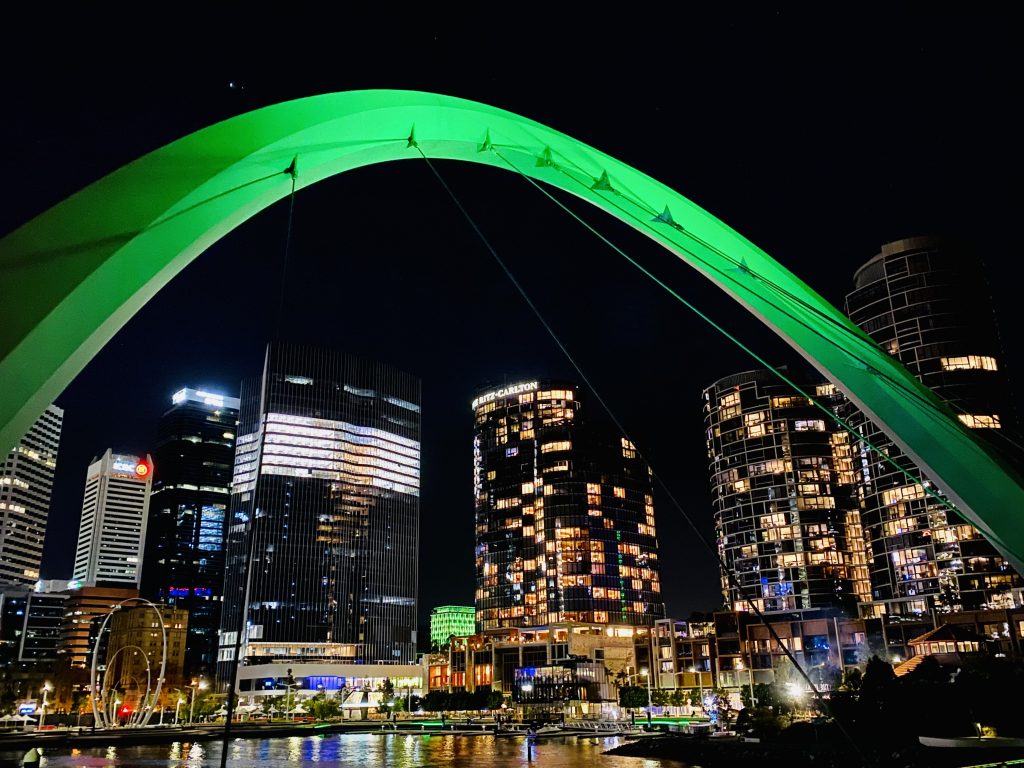 A bridge illuminated in green with city lights behind it.