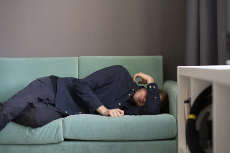 A man sleeping on the couch, his face is partially covered by his arm.