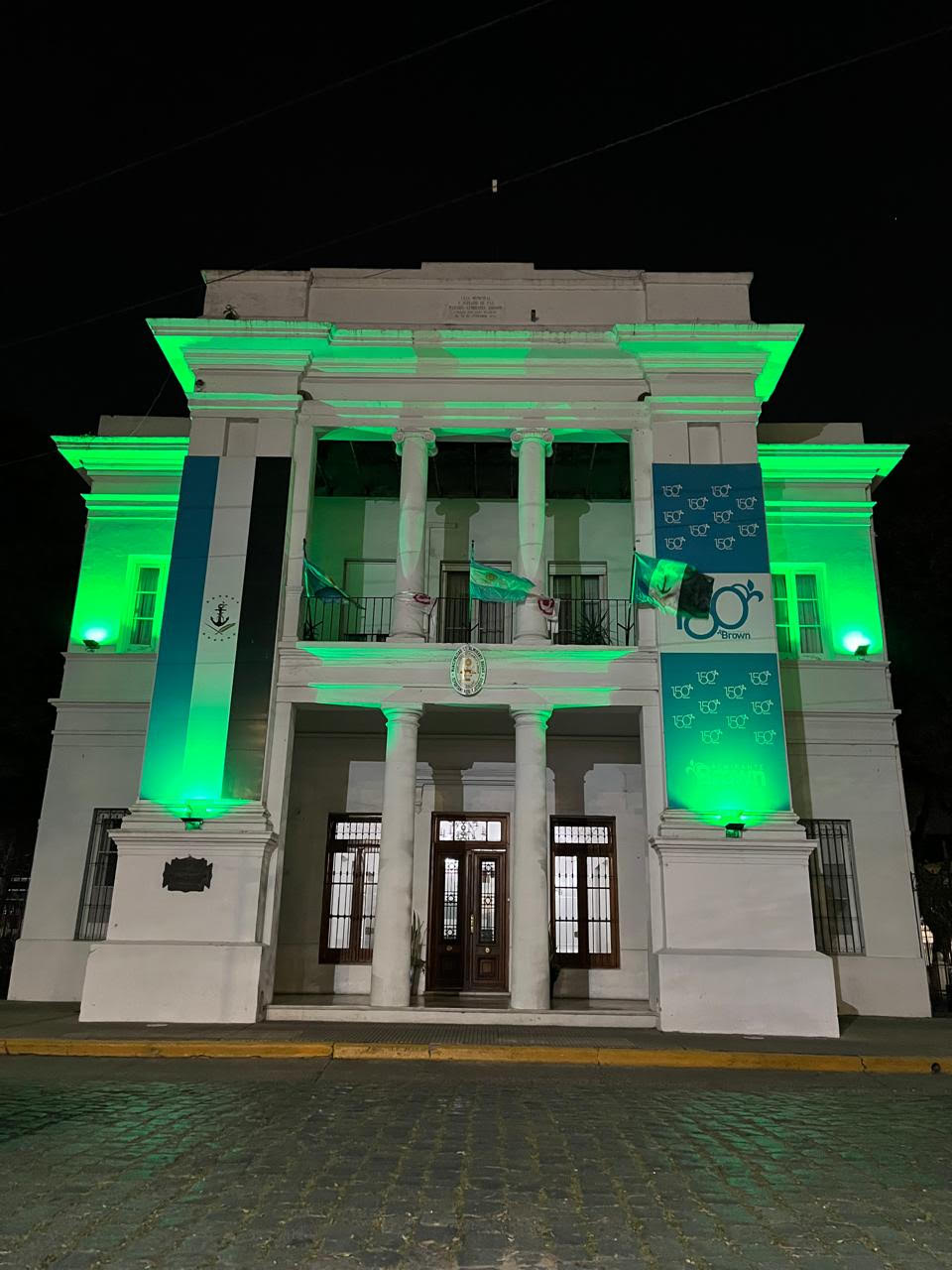 White building with with columns up front lit in mito green