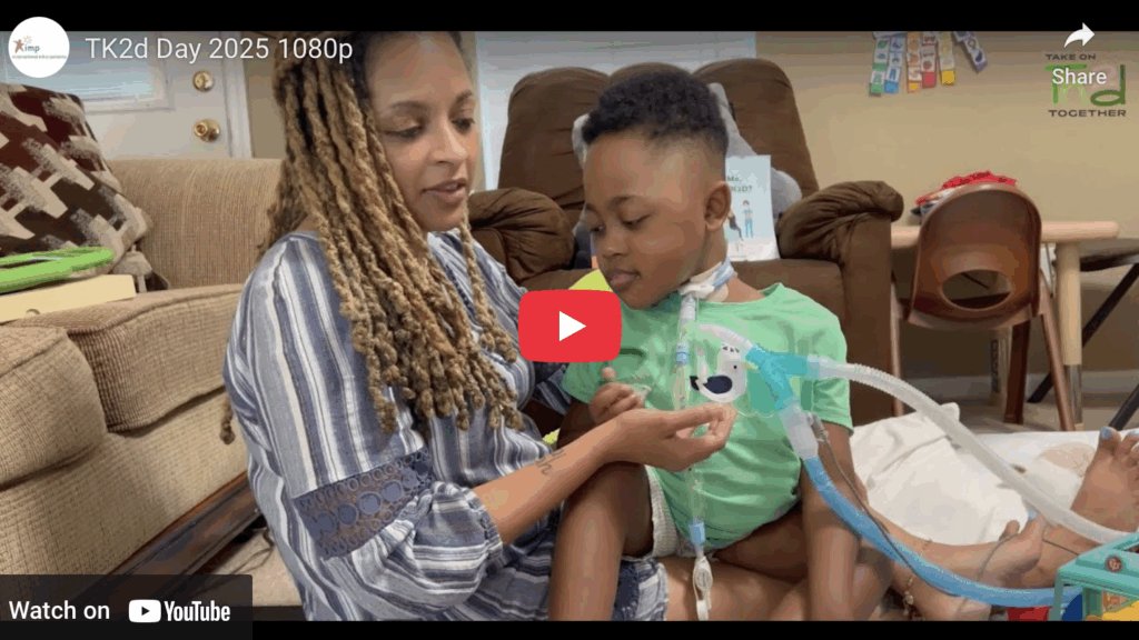 Image of a mother with long blonde dreadlocks holding a child with short black hair on her lap who is attached to a breathing machine