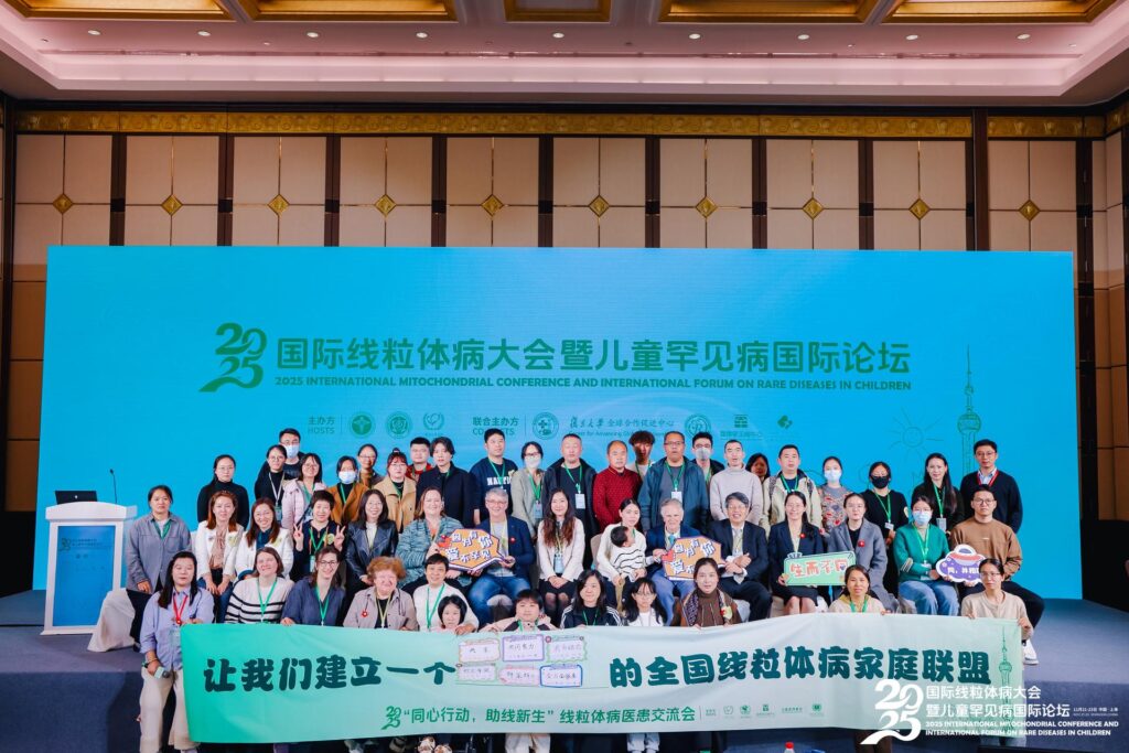 Group of about 60 conference participants standing on a stage with signage in front and behind them in Chinese. The group includes IMP Board Member Kristen Clifford and other participants of the 2025 International Mitochondrial Conference and the First International Forum on Rare Diseases in Children in Shanghai this November