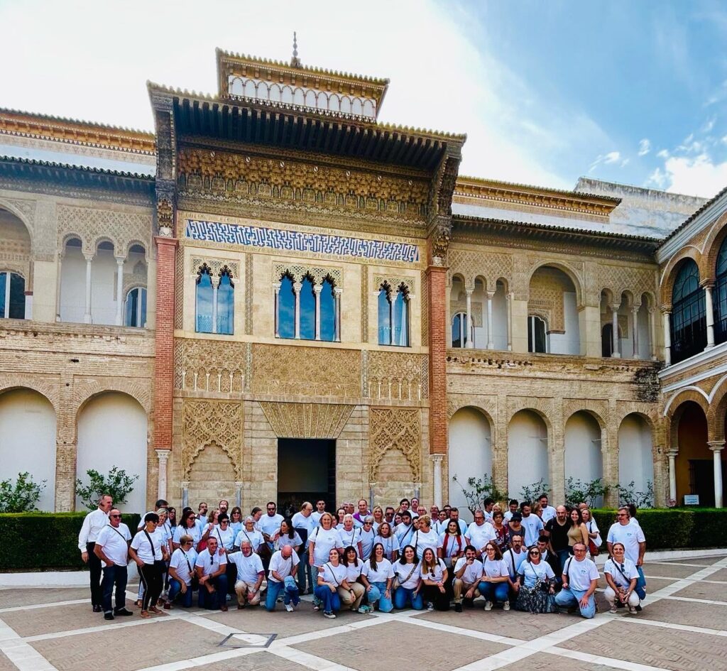 Photo of a large group of people related to ASANOL. They are wearing jeans and white t-shirts and are crouching or standing in front of an impressive Moorish style building. 